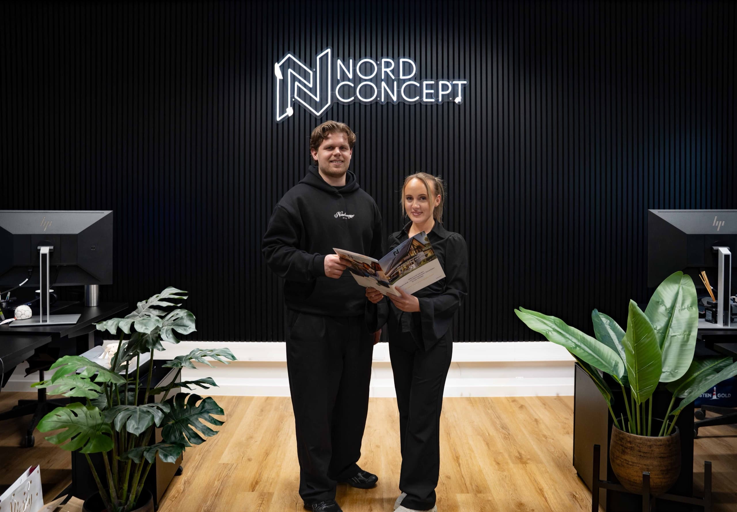 Zwei NordConcept GmbH Mitarbeiter vor NordConcept-Logowall im modernen Showroom-Empfang