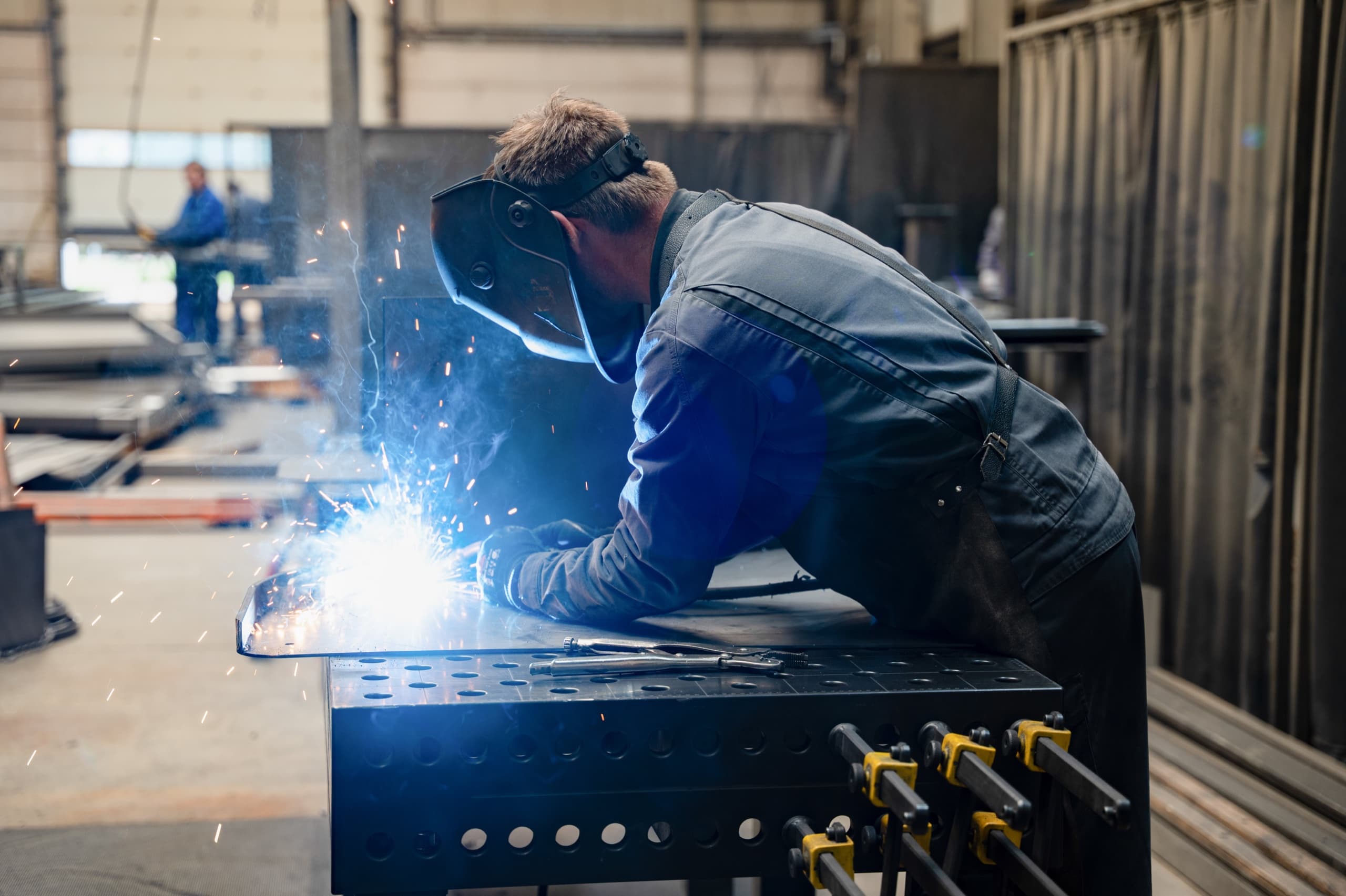 AXA Schweißer mit Helm schweißt Metallkonstruktion, Lichtbogen-Funken sichtbar