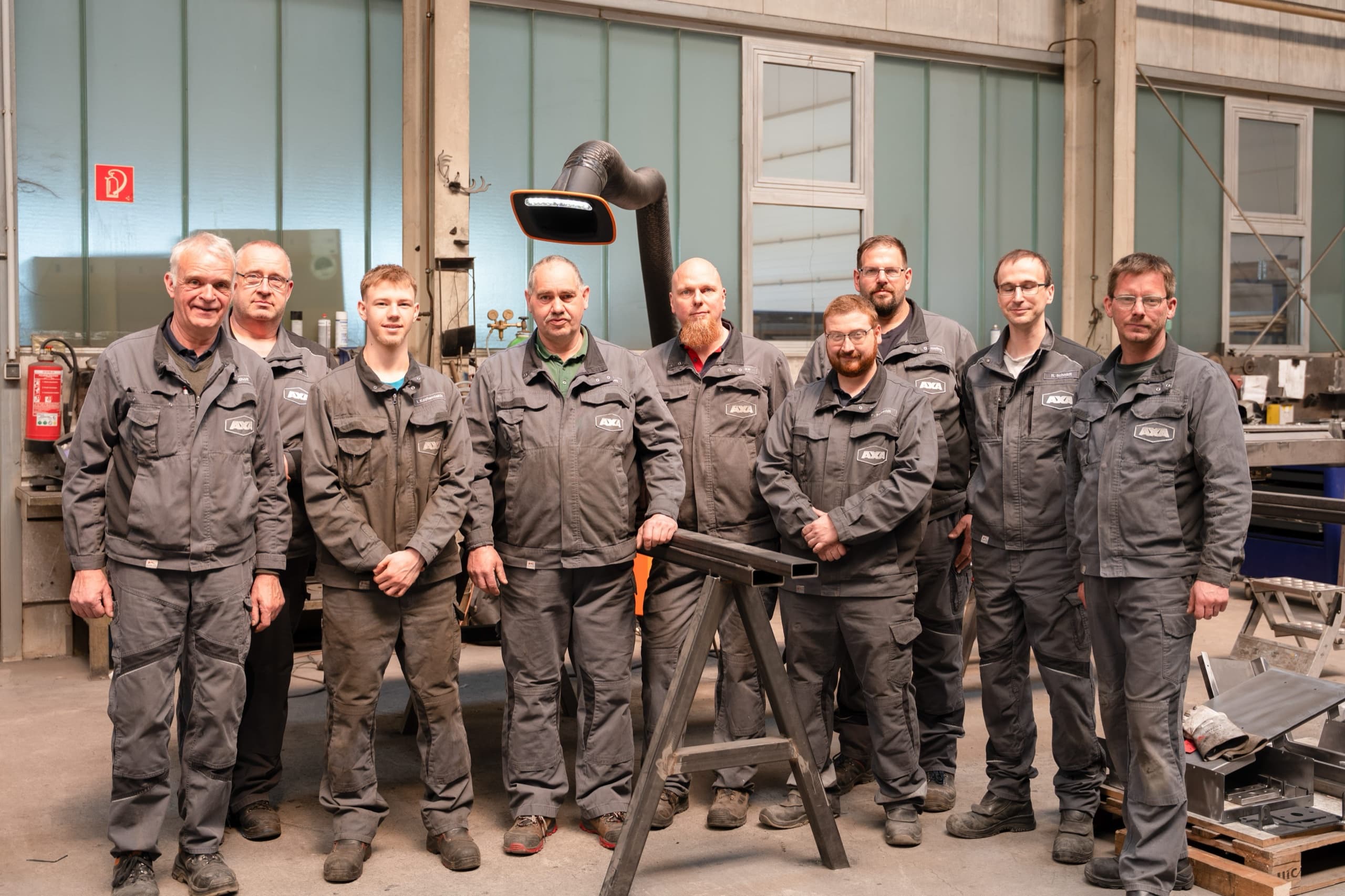 Acht AXA Schlosser und Metallbauer in Montageanzügen in der Produktionshalle