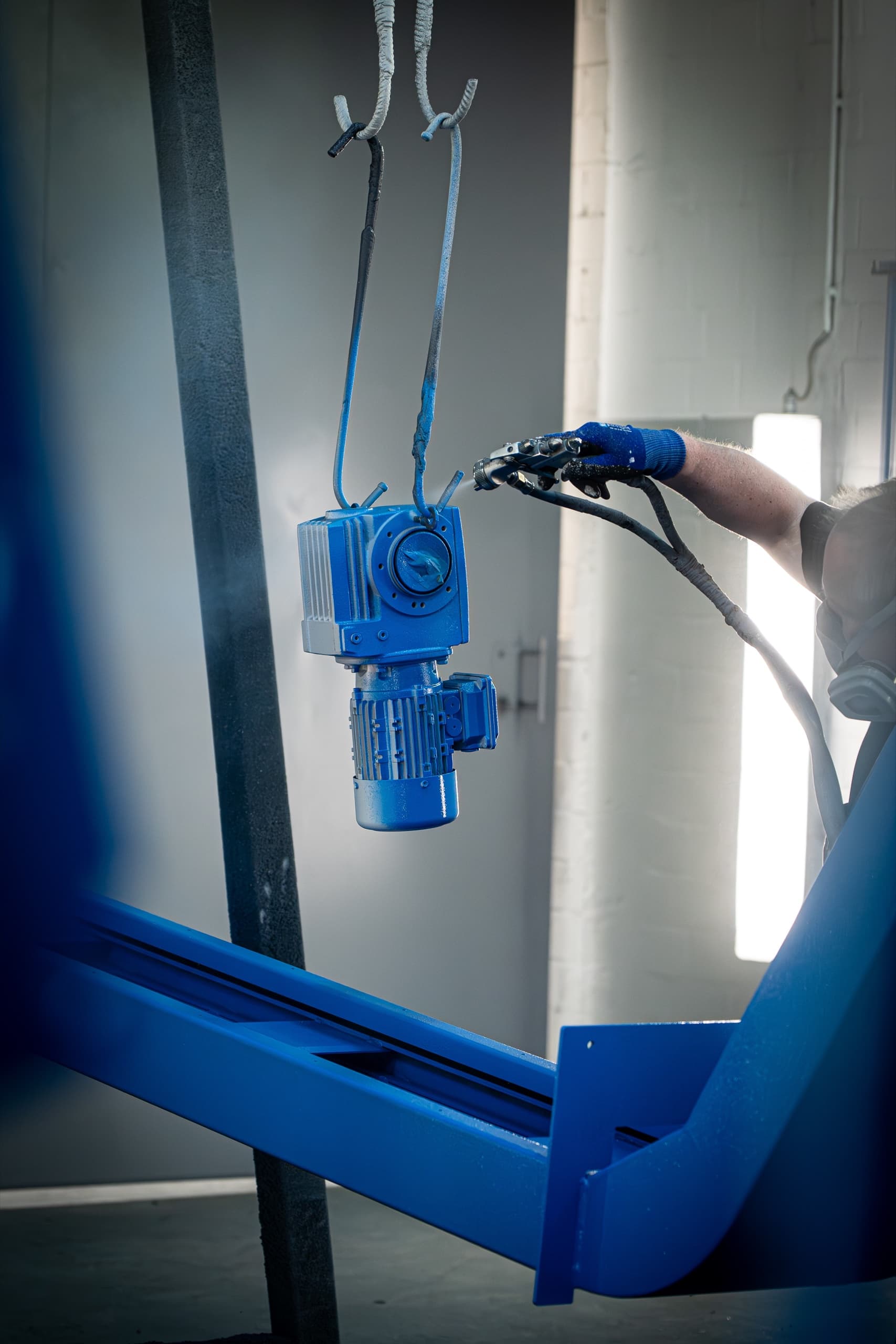 AXA Lackierer sprüht blaue Farbe auf Getriebemotor in der Lackierkabine