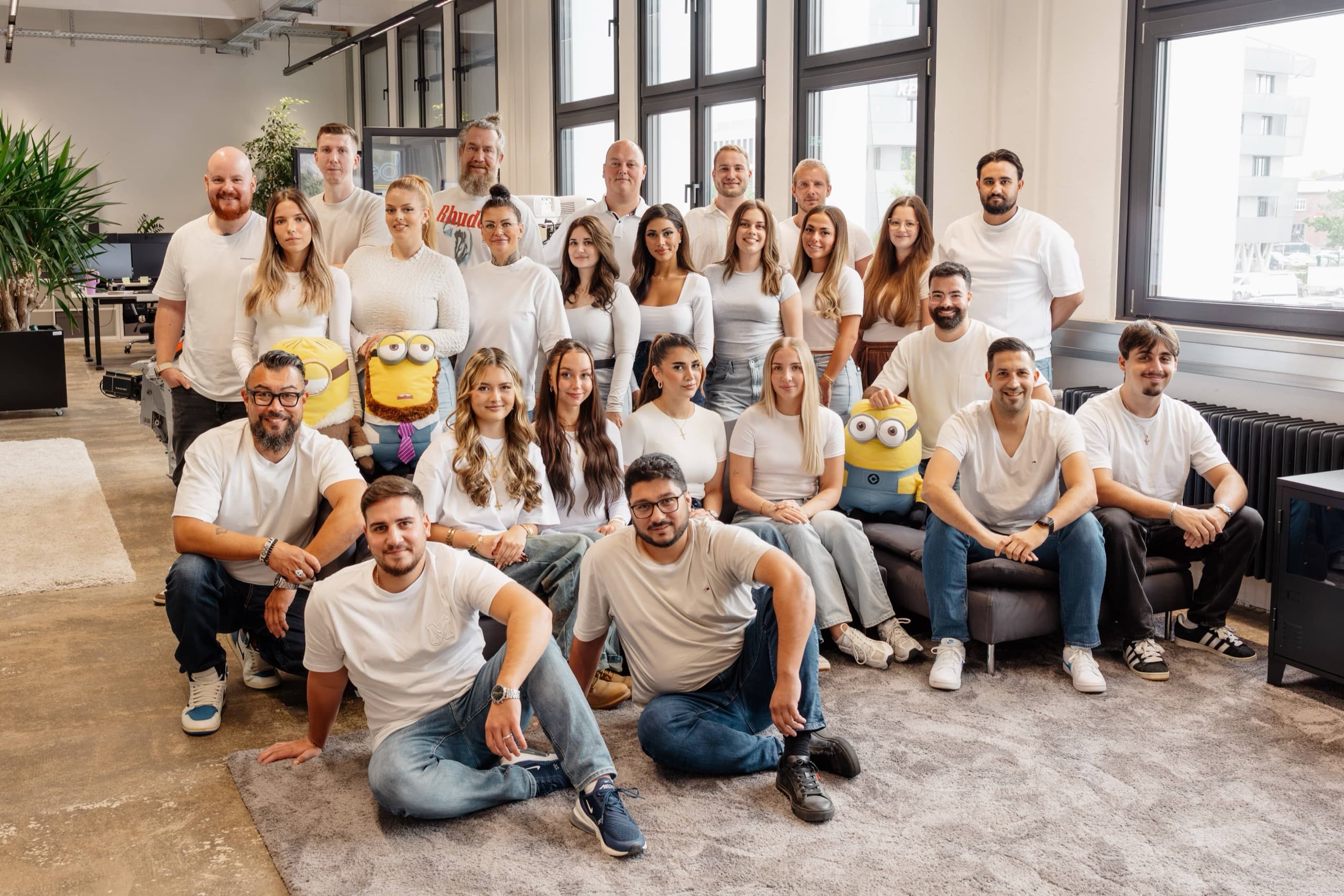 Großes bee-doo Gesamtteam (~22 Personen) im modernen Loft-Büro mit Minion-Figuren