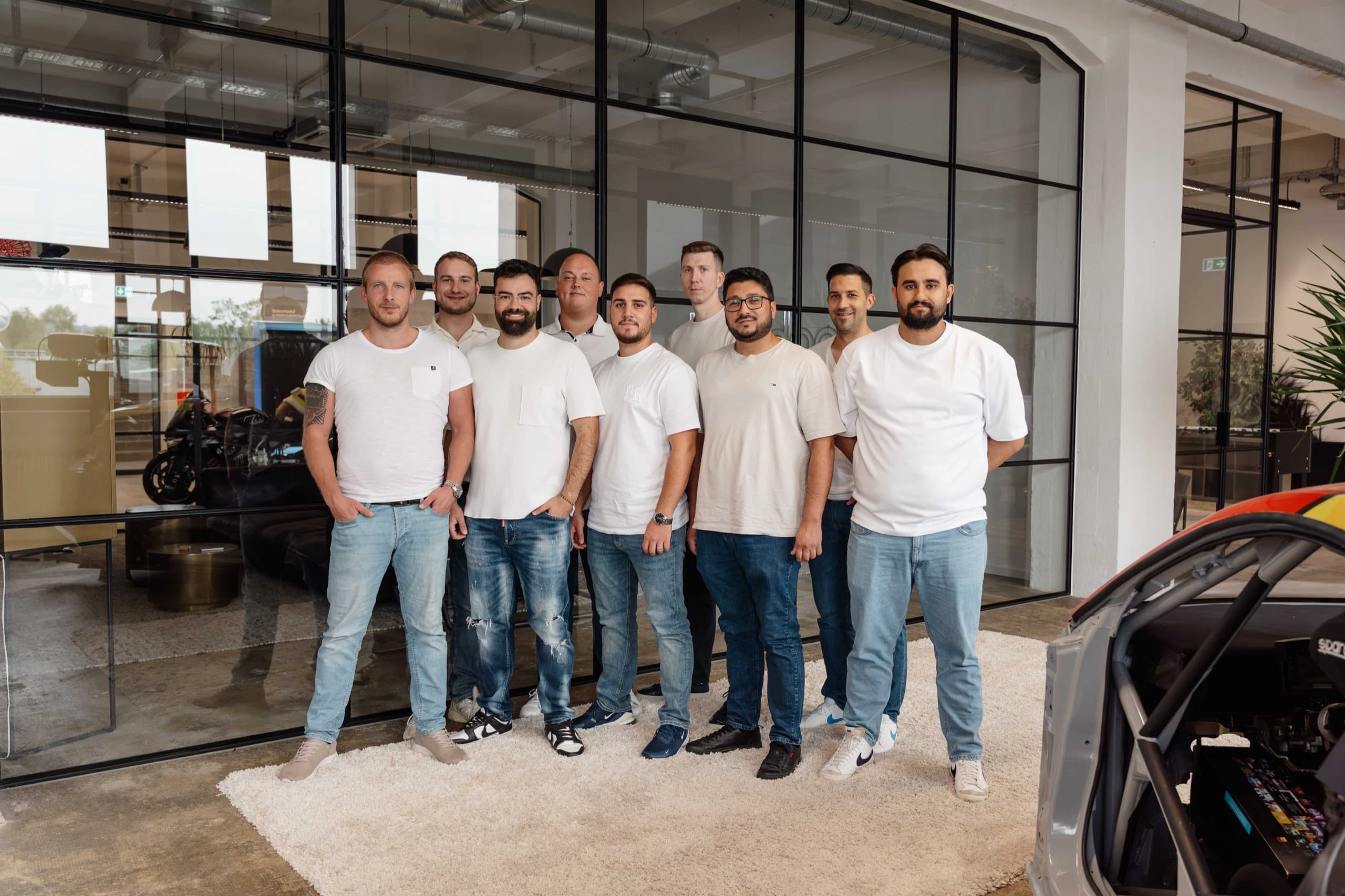 Neun bee-doo Mitarbeiter in Weiß vor Glasfront-Fassade, Männer-Team-Foto