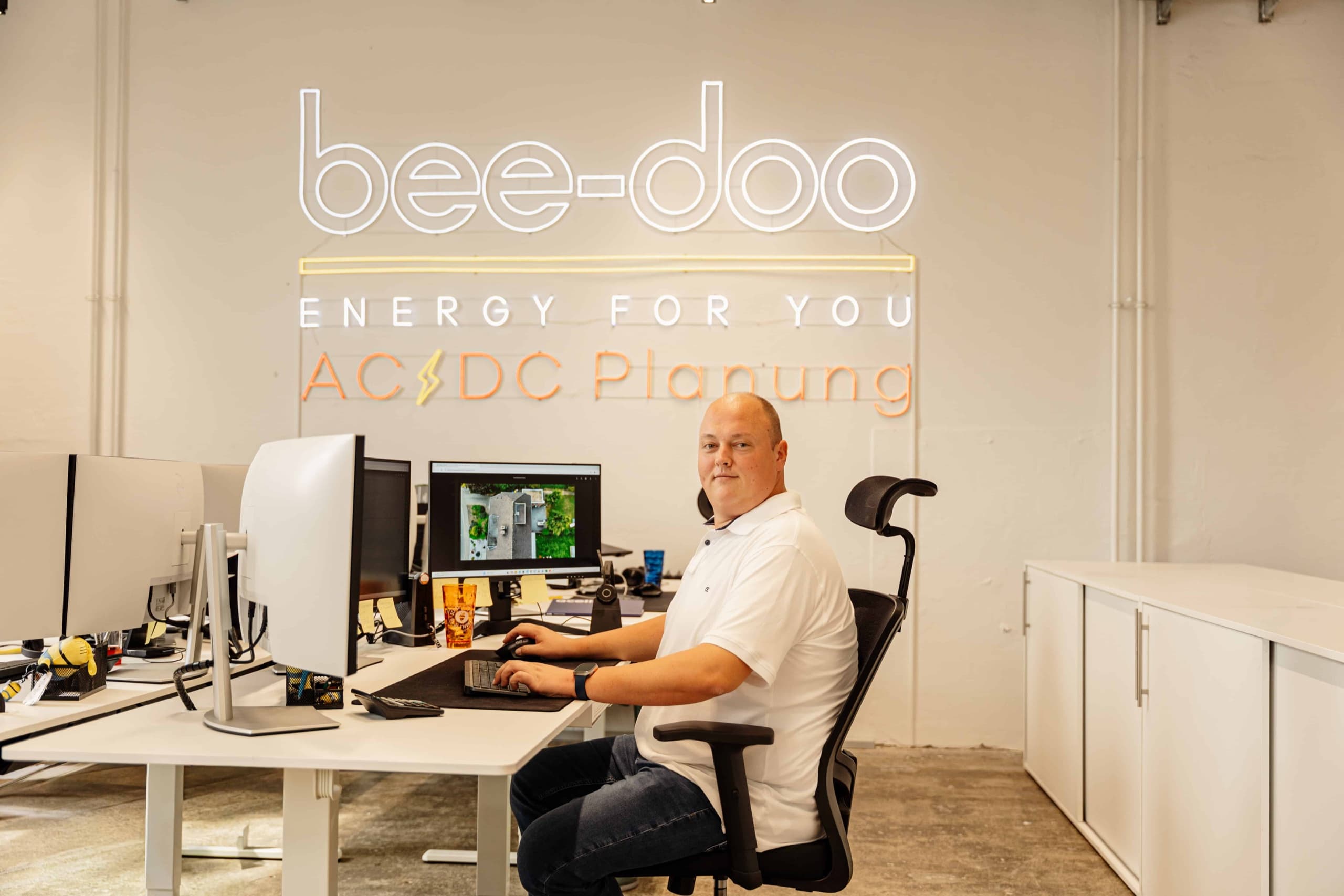 bee-doo Mitarbeiter am Schreibtisch mit bee-doo ENERGY FOR YOU AC/DC Wandlogo