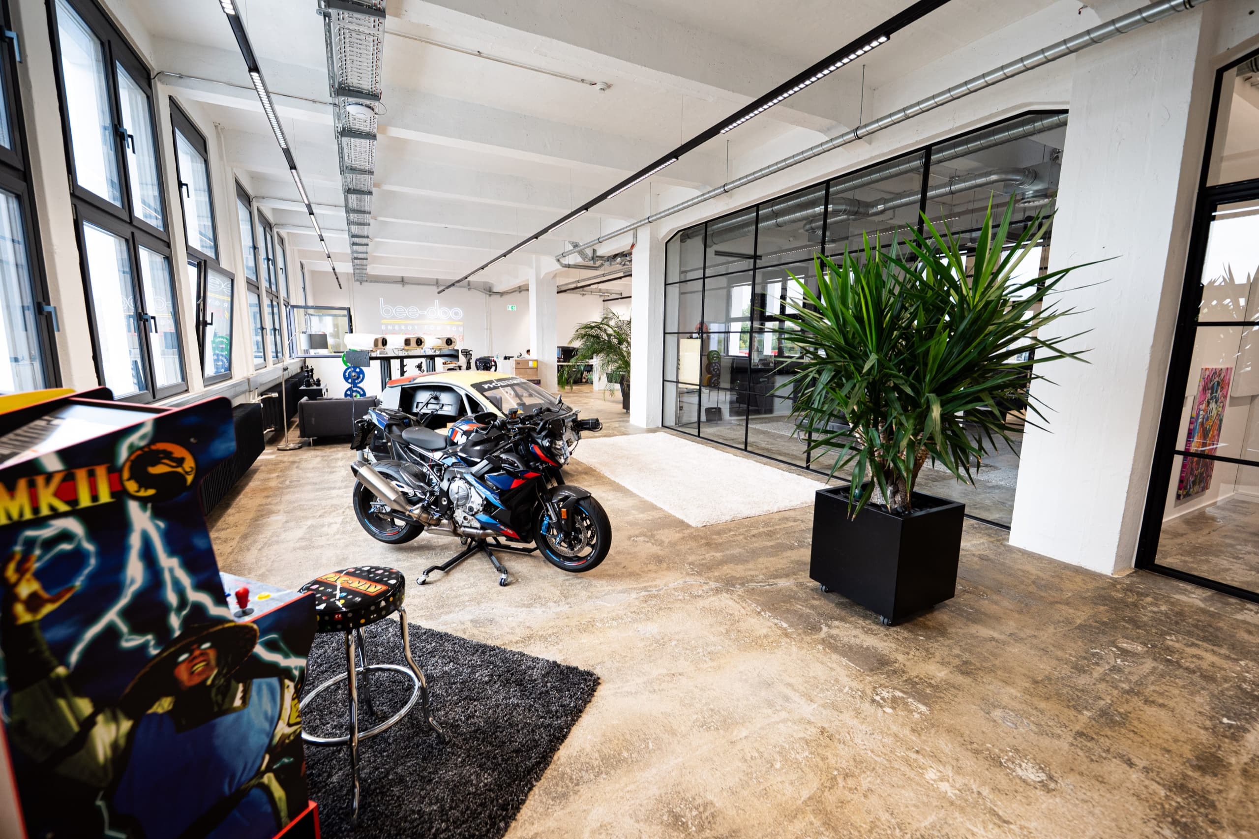 Modernes bee-doo Büro mit Motorrad als Deko-Element, Arcade-Automat und Glastrennwänden