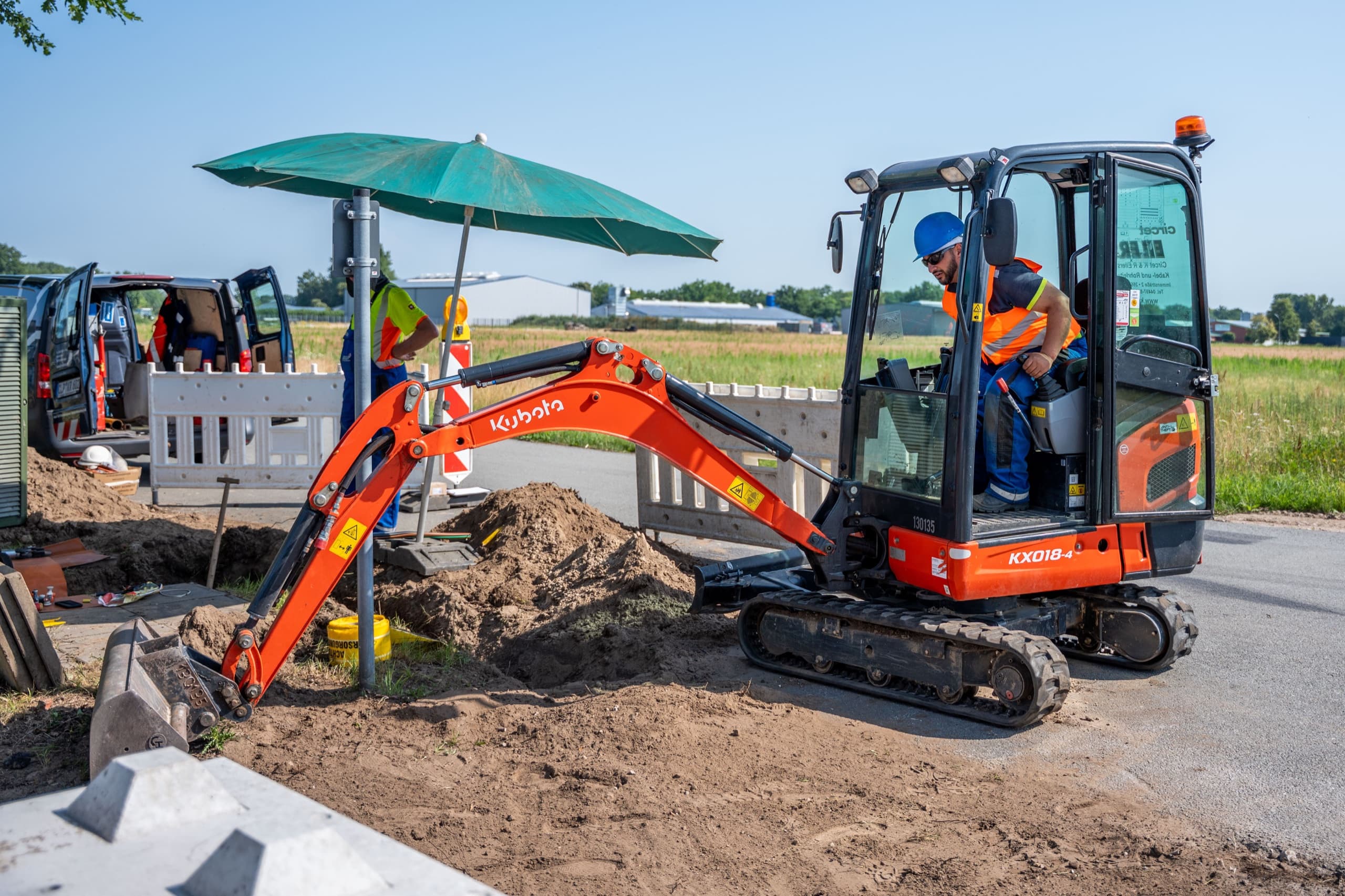 Monteur in oranger Warnweste bedient Kubota KX018-4 Minibagger am Straßenrand