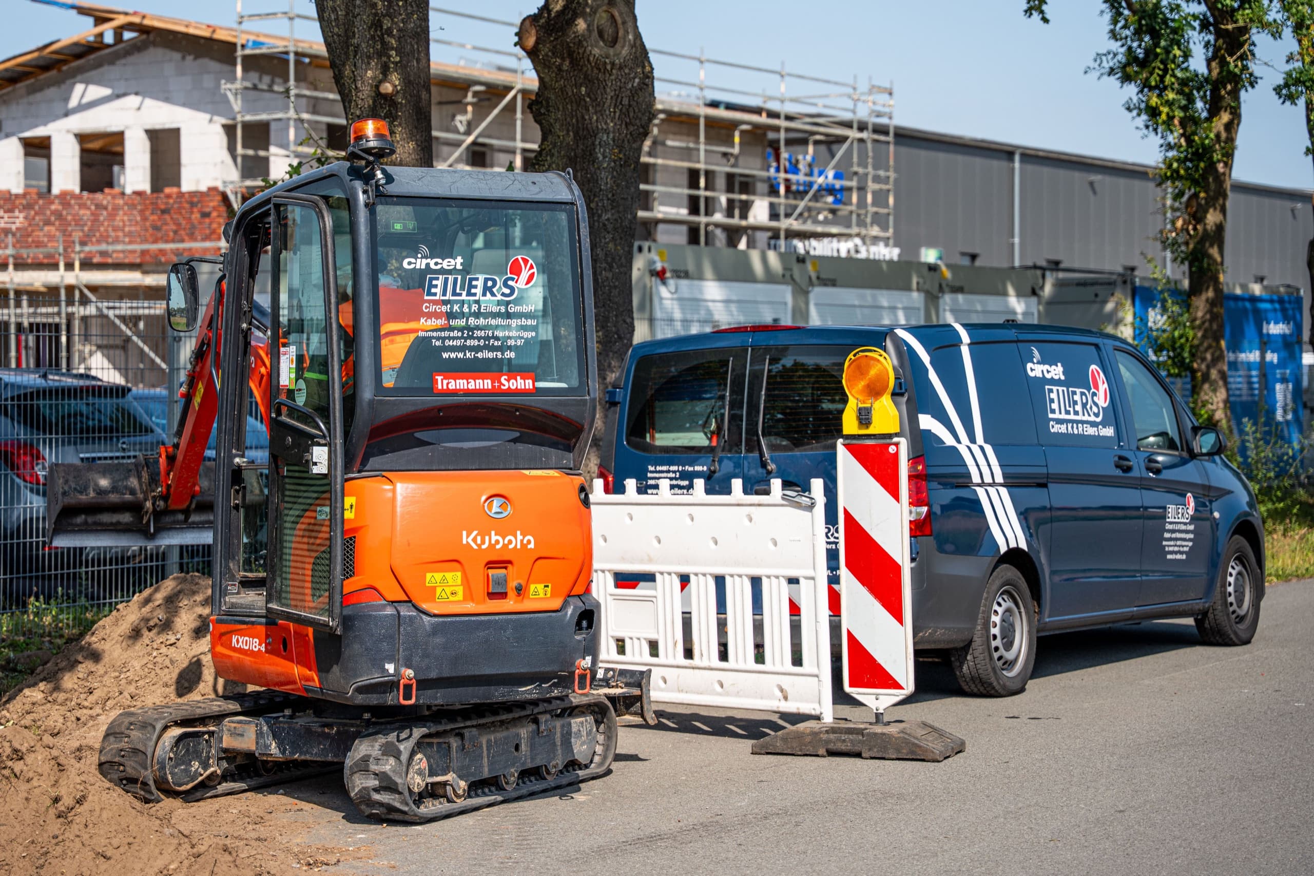 Oranger Kubota Minibagger und blauer Eilers-Transporter an Straßenbaustelle