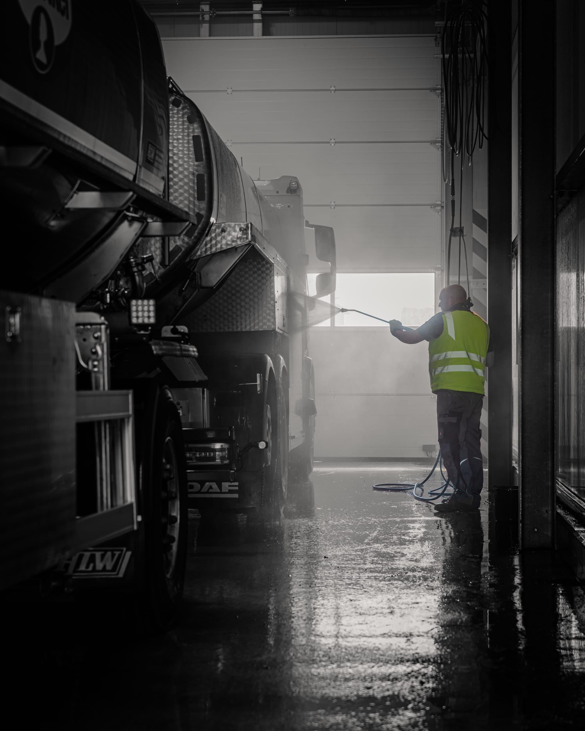 Atmosphärenbild in Schwarzweiß: Mitarbeiter in Warnweste reinigt DAF Tanklastzug in Waschhalle