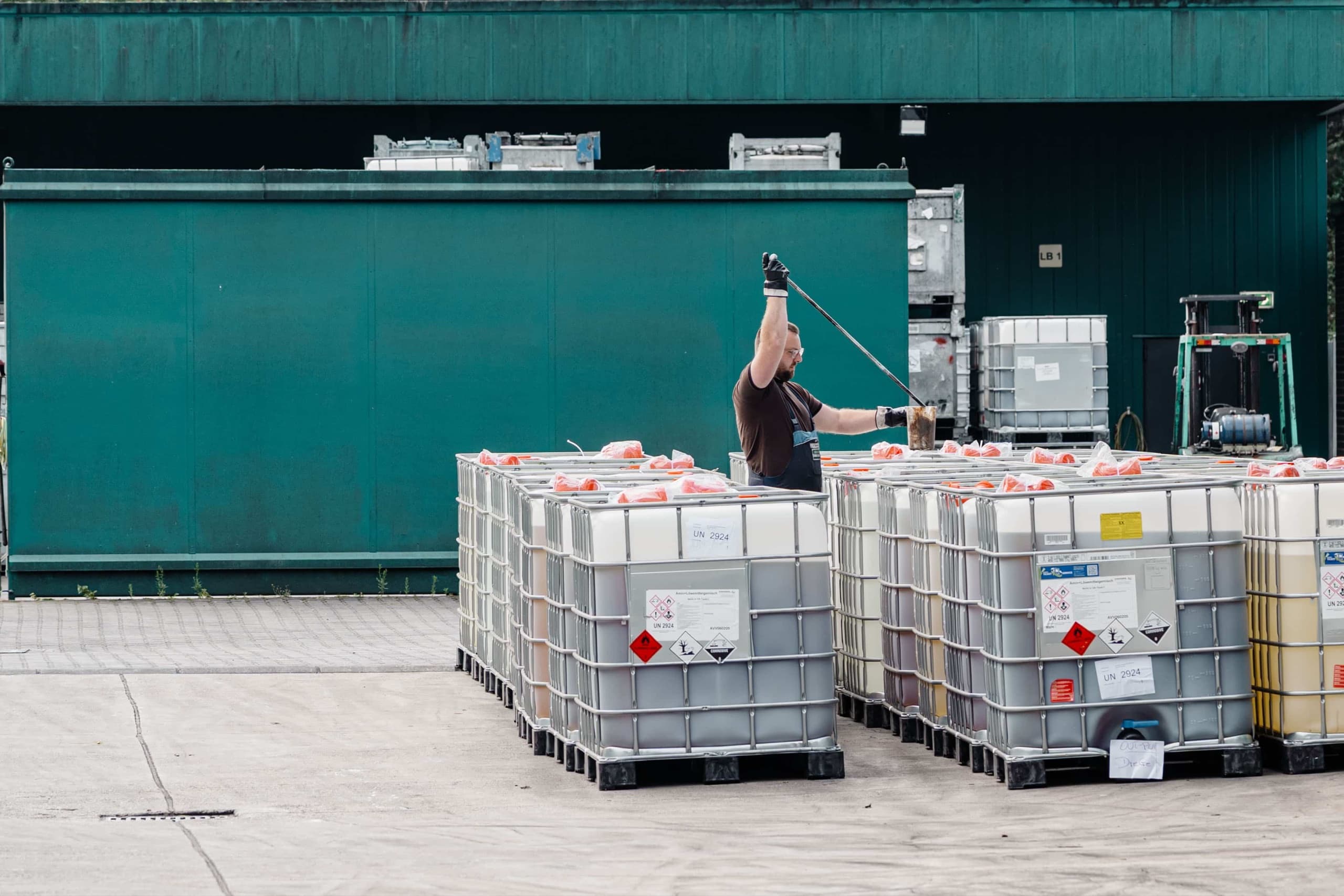 Drekopf Mitarbeiter reinigt IBC-Gefahrstoffcontainer mit Hochdrucklanze vor grüner Lagerhalle