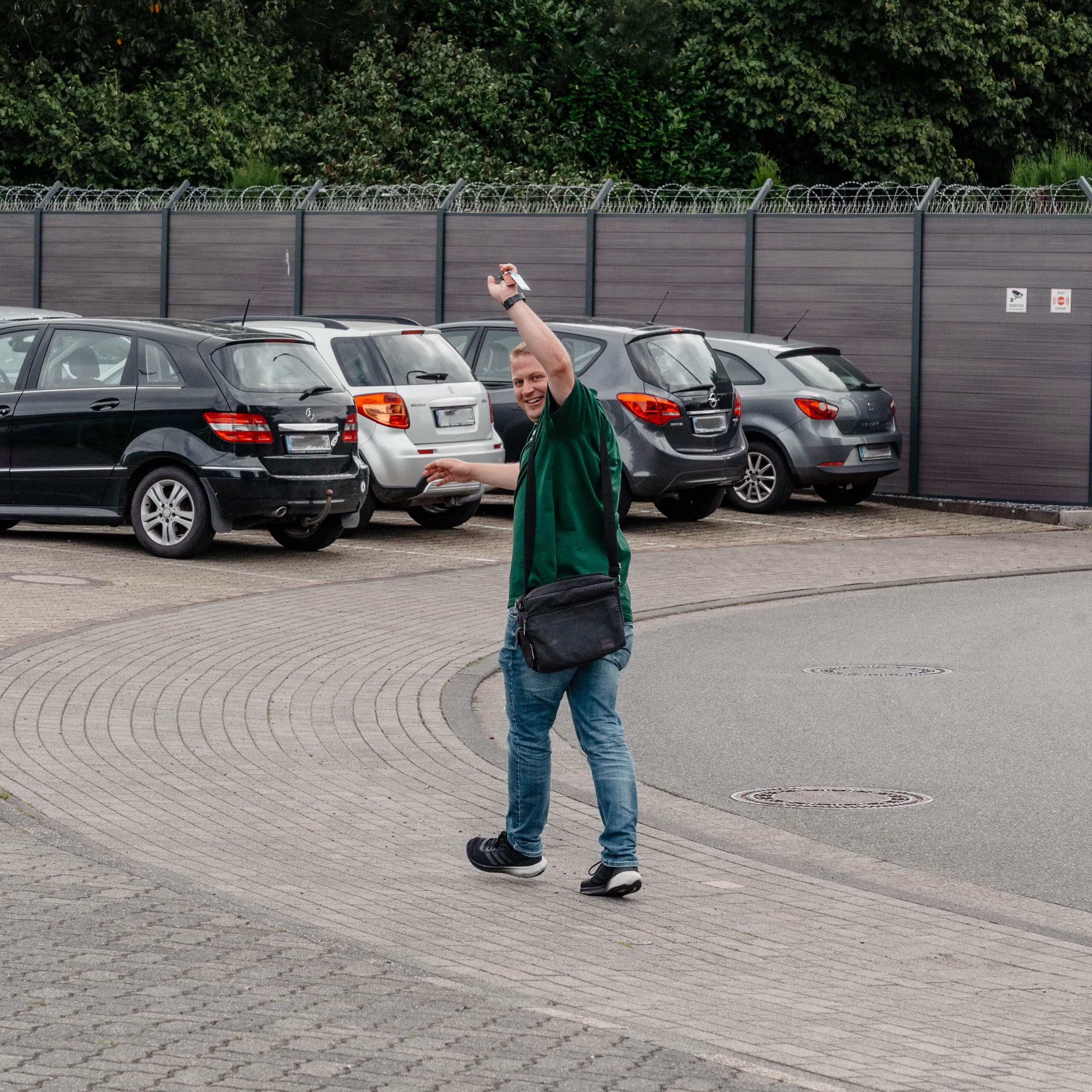Drekopf Mitarbeiter in grünem Polo winkt grüßend über den Firmenparkplatz