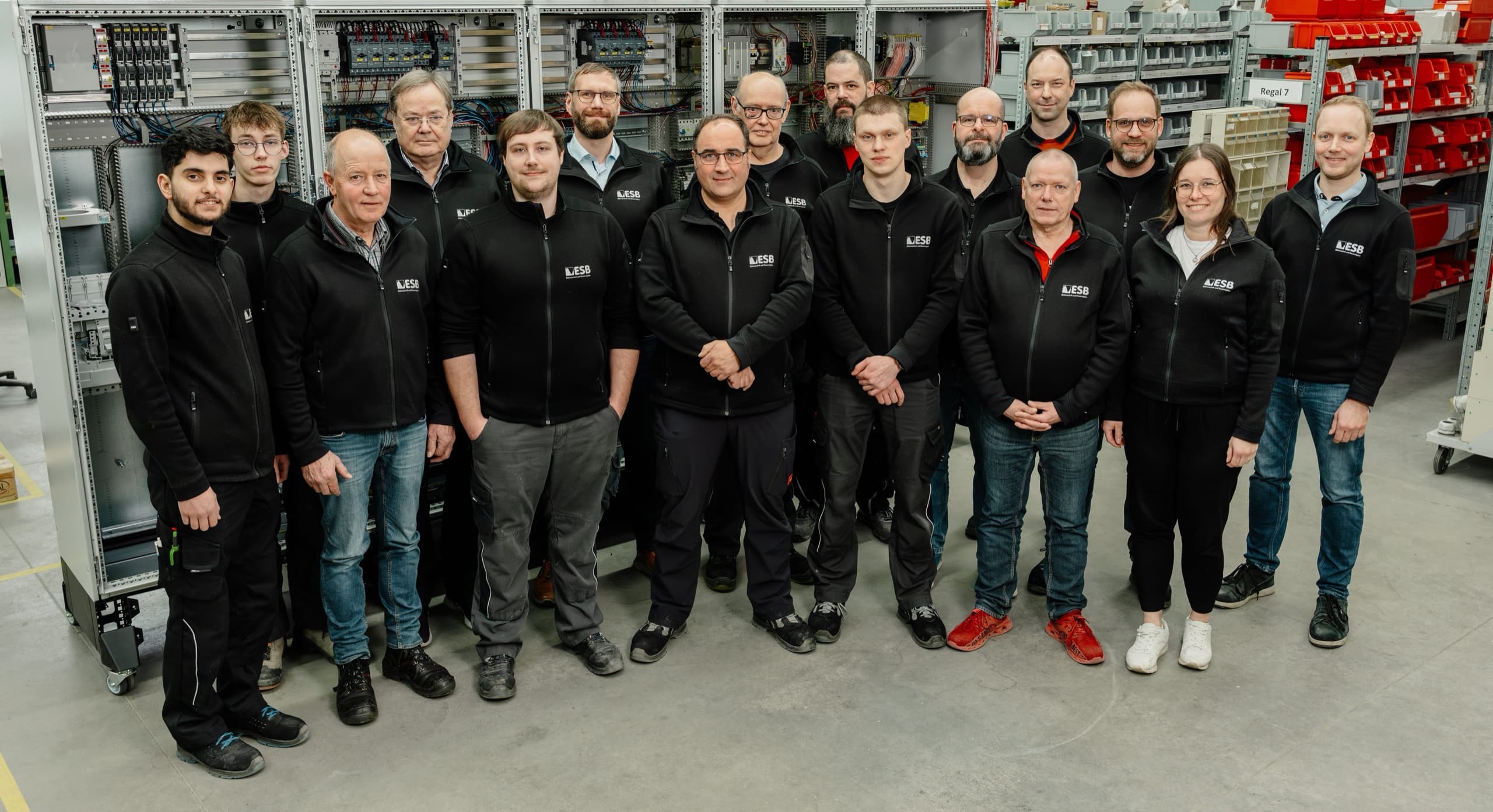 ESB Elektrotechnik Gesamtteam (~16 Personen) in schwarzen ESB-Firmenjacken vor fertigem Schaltschrank