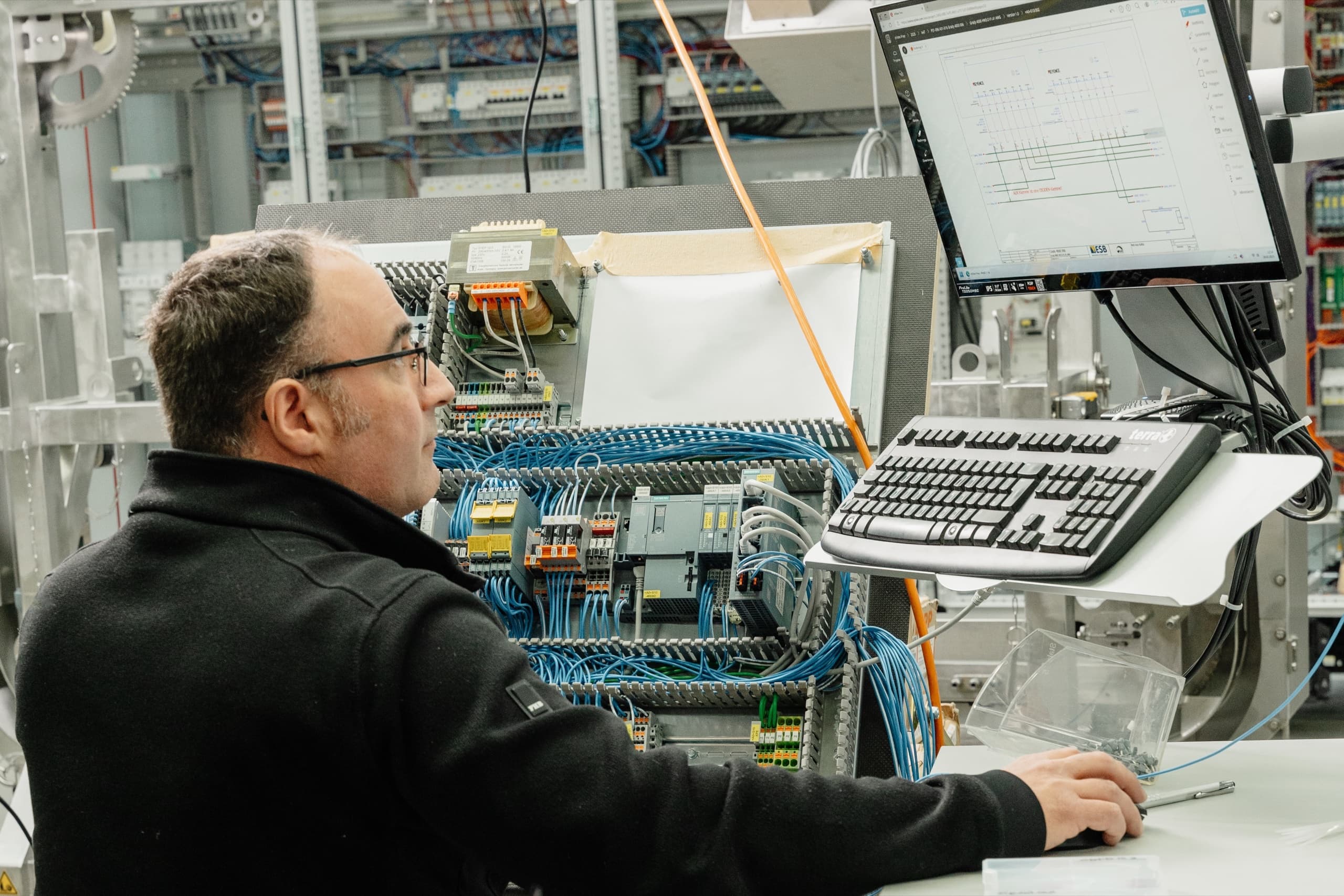 ESB Elektriker programmiert an Industrie-Terminal vor fertigem Steuerungsschrank