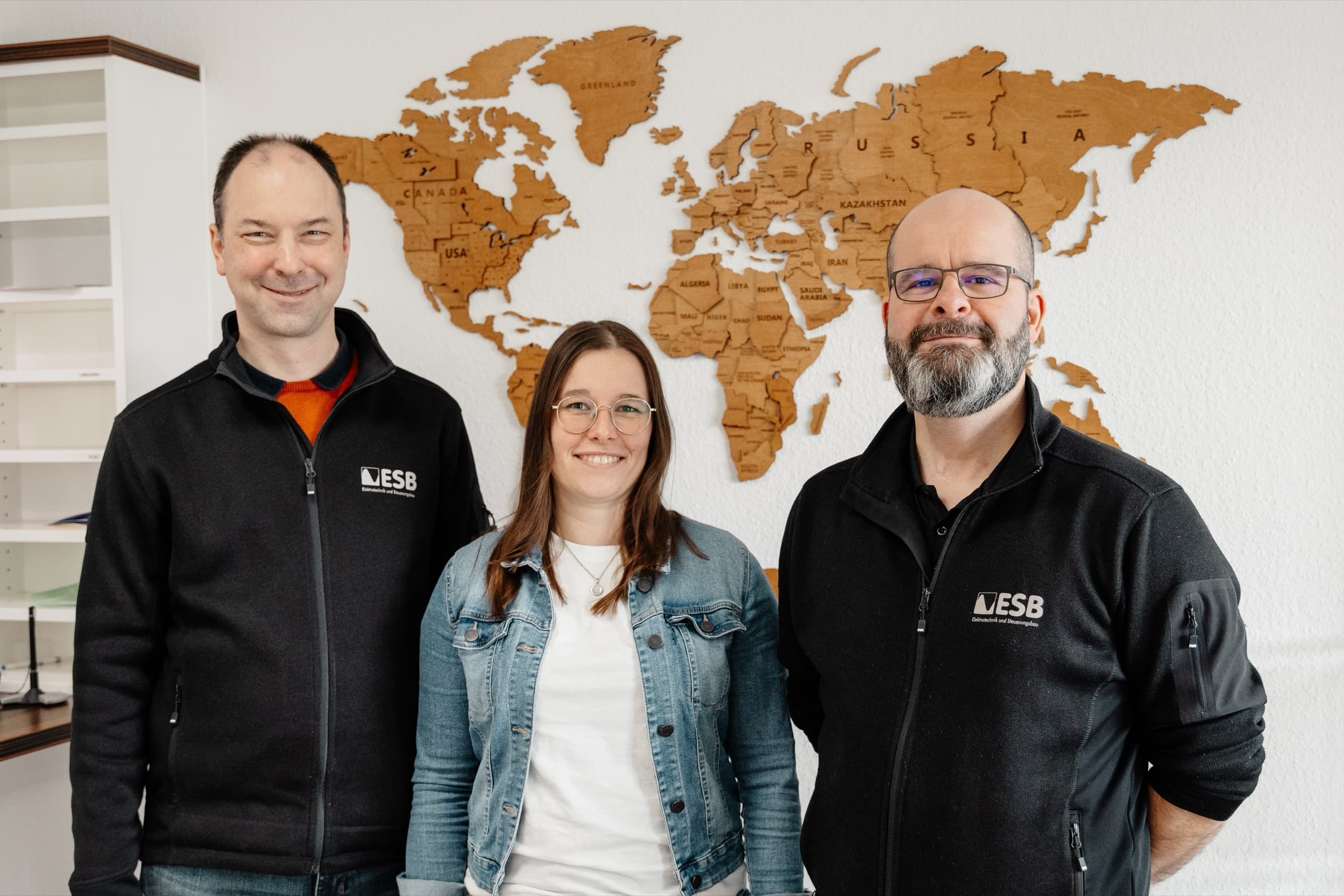 Drei ESB Mitarbeitende im Büro vor Weltkarte, entspannte Team-Aufnahme