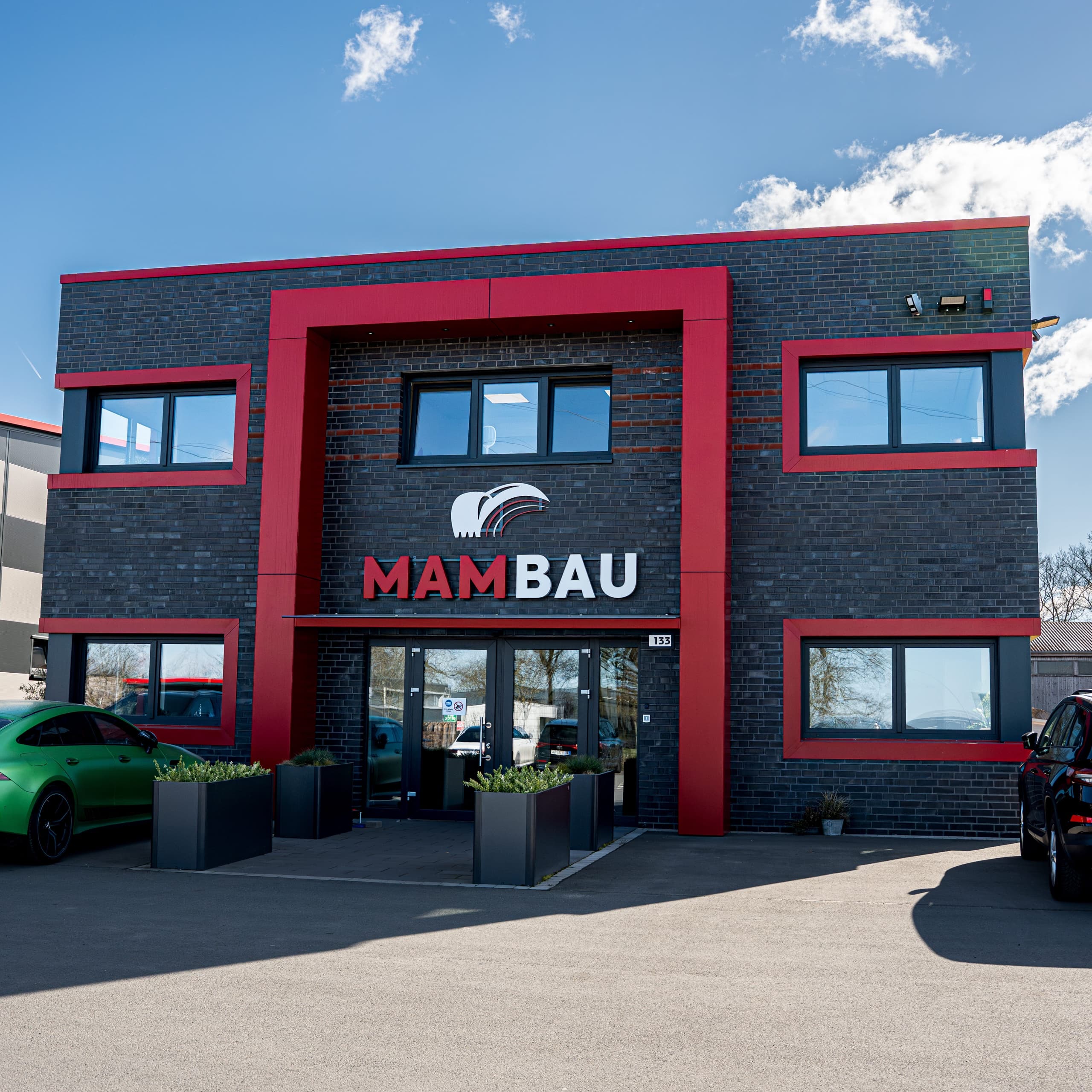 MAM-BAU Firmensitz Frontansicht mit MAMBAU-Logo, schwarze Klinkerfassade und roter Rahmung