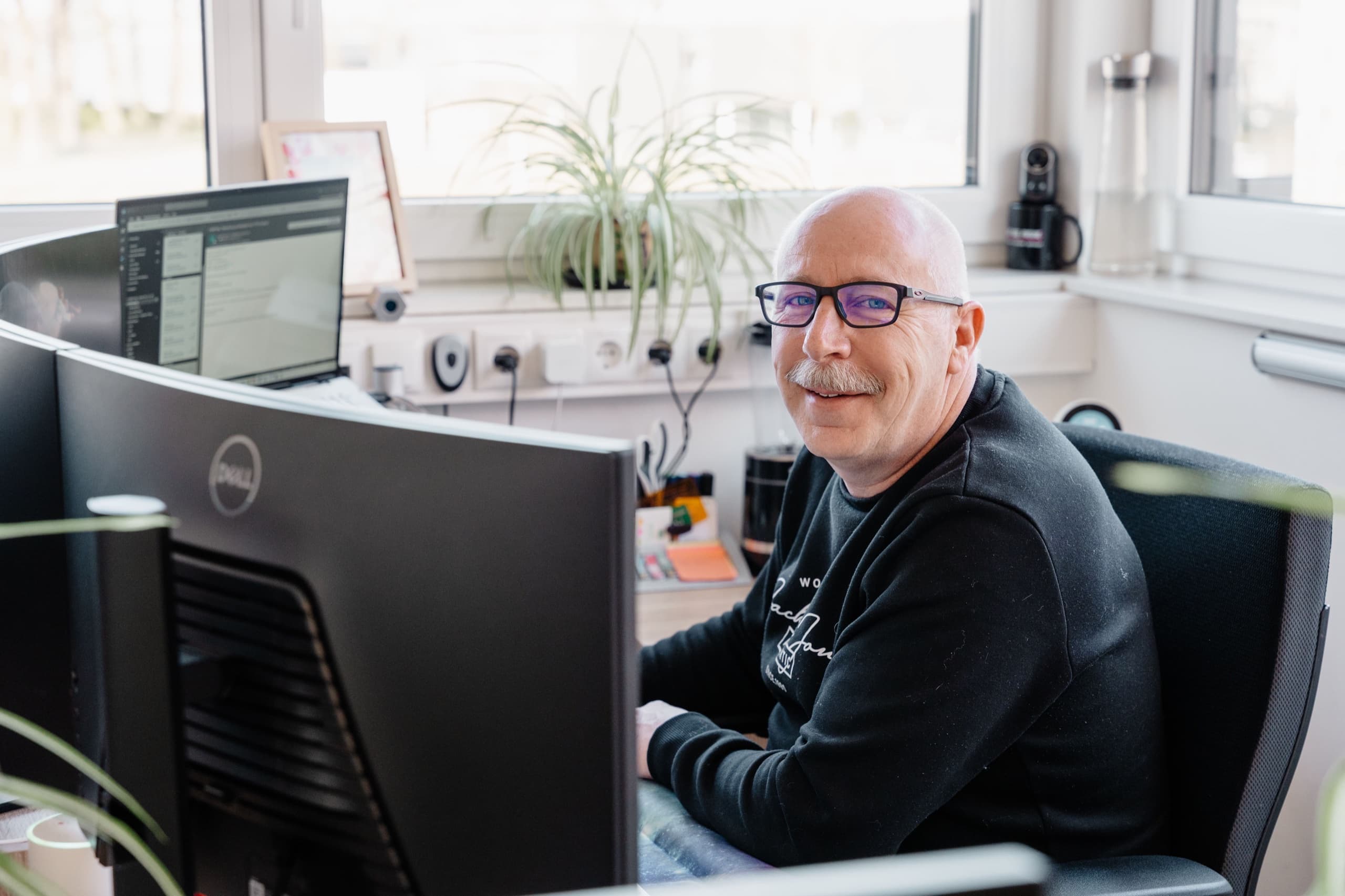 MAM-BAU Mitarbeiter lächelt am Dell Curved-Monitor in seinem Büro