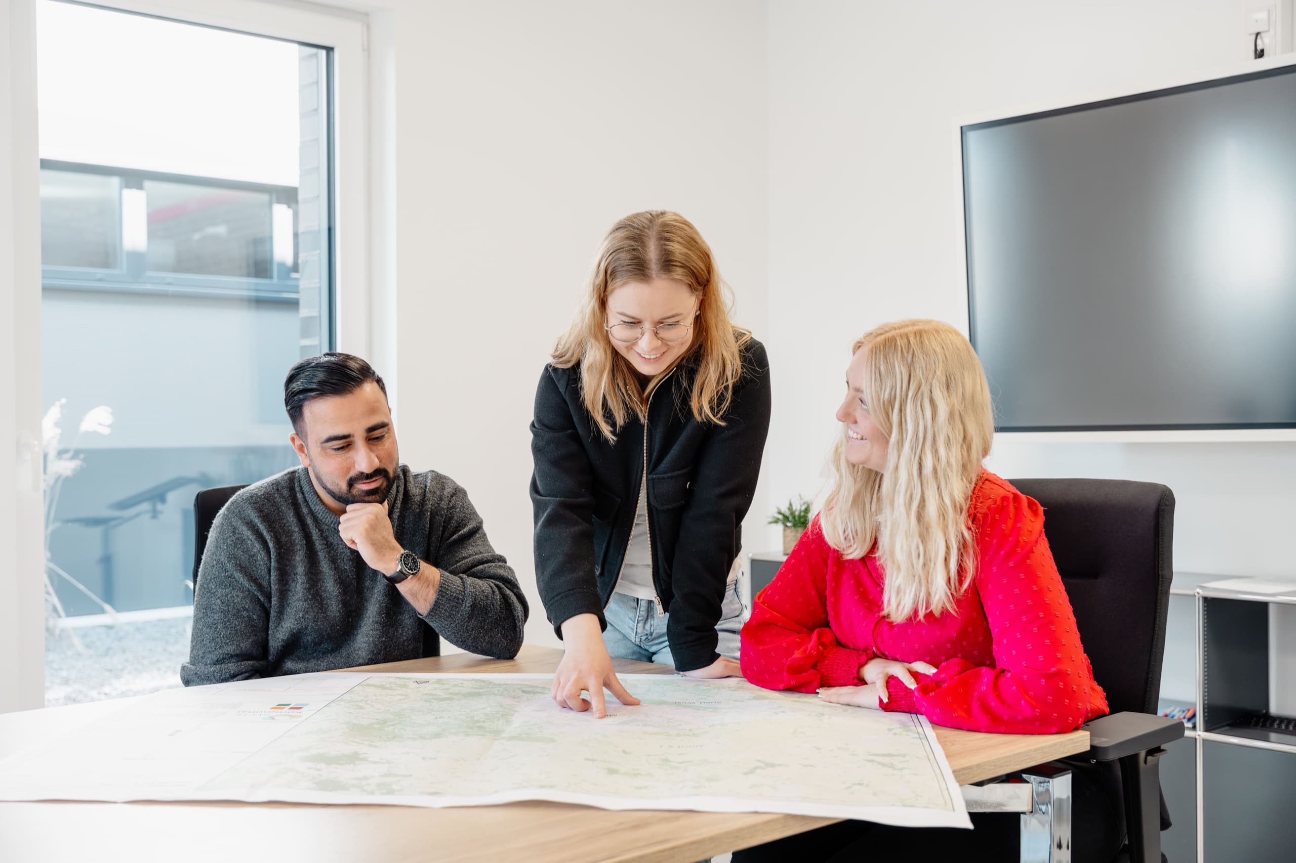 Drei MAM-BAU Mitarbeitende im Besprechungsraum bei Projektplanung über Landkarte