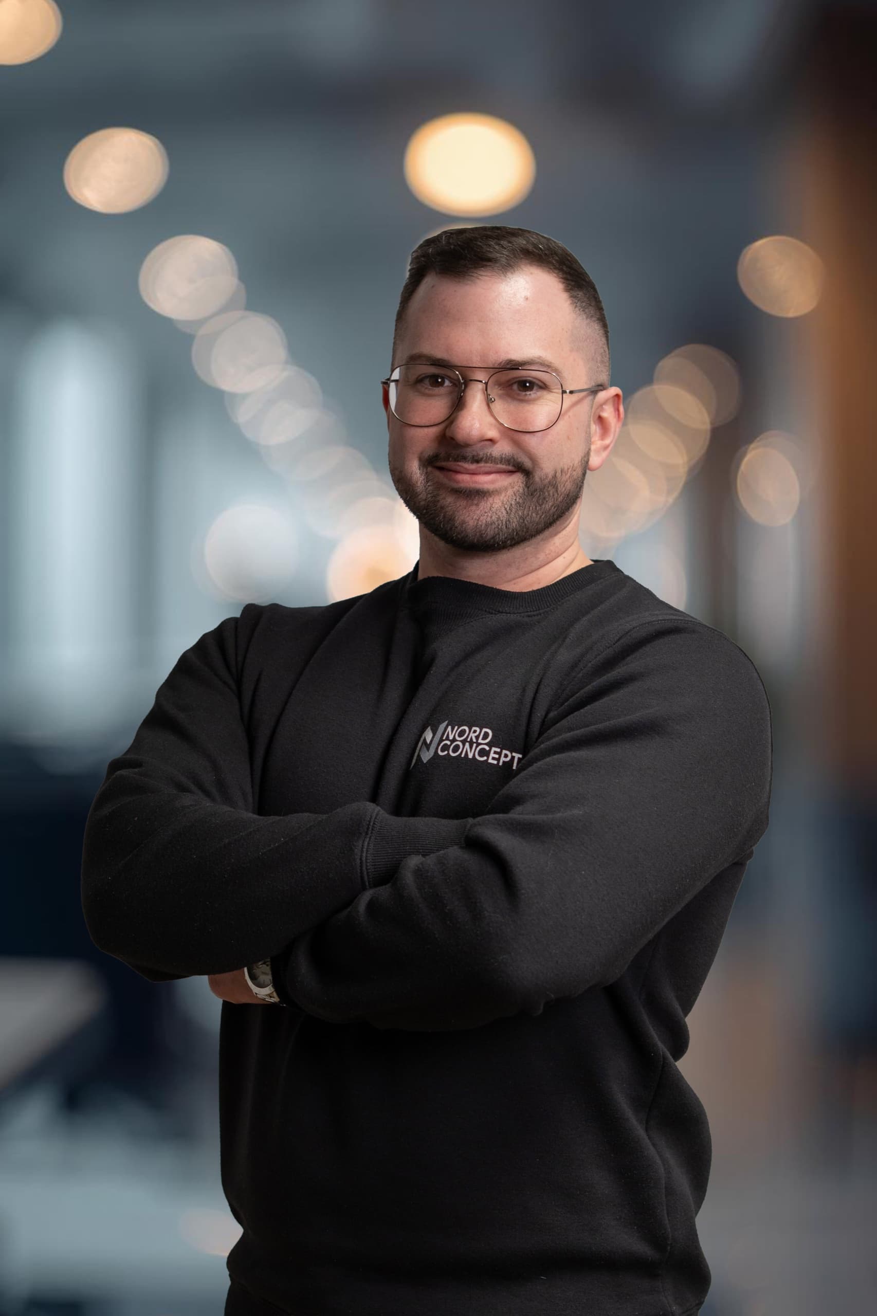 Marco – NordConcept GmbH Mitarbeiter in schwarzem NordConcept-Sweatshirt mit Brille, Businessportrait