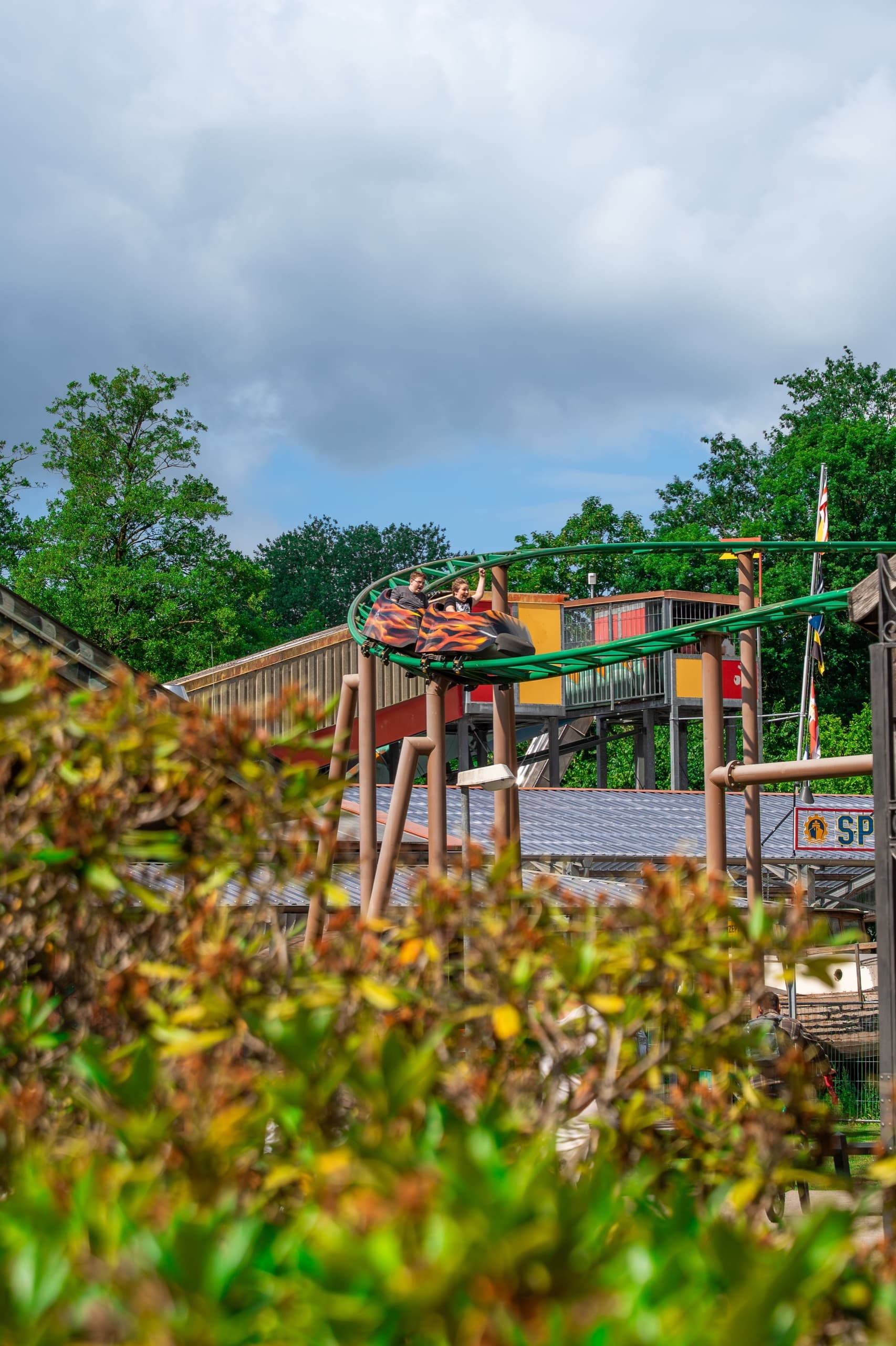 Achterbahn-Wagon mit Flammen-Design fährt durch grüne Baumlandschaft im Freizeitpark Schloss Dankern