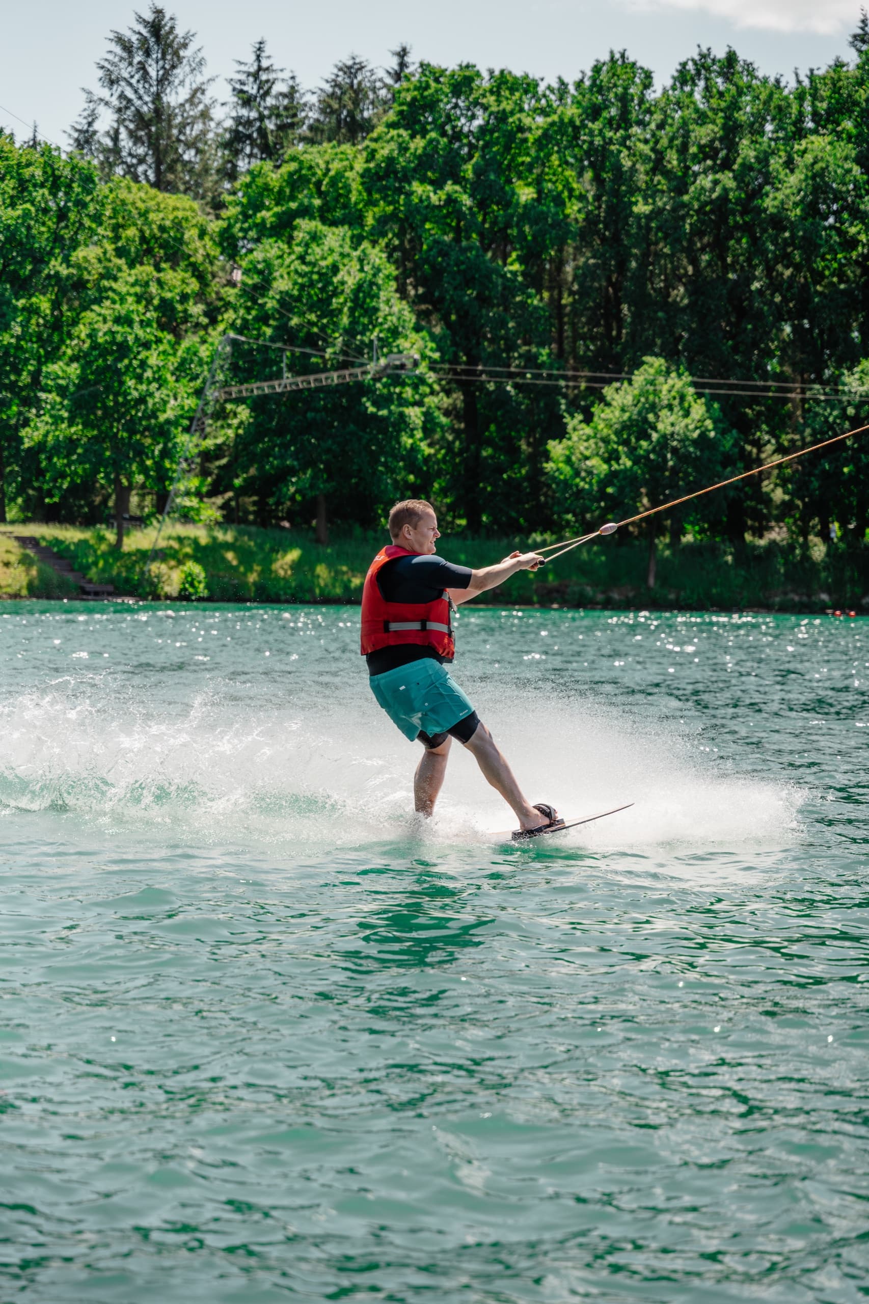 Wakeboarder mit roter Weste fährt auf türkisem See am Schloss Dankern Wakepark