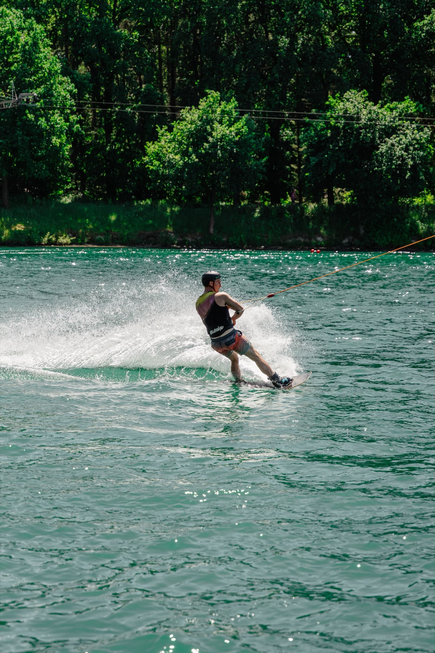 Wakeboarder von hinten surft über den türkisfarbenen See des Schloss Dankern Wakeparks