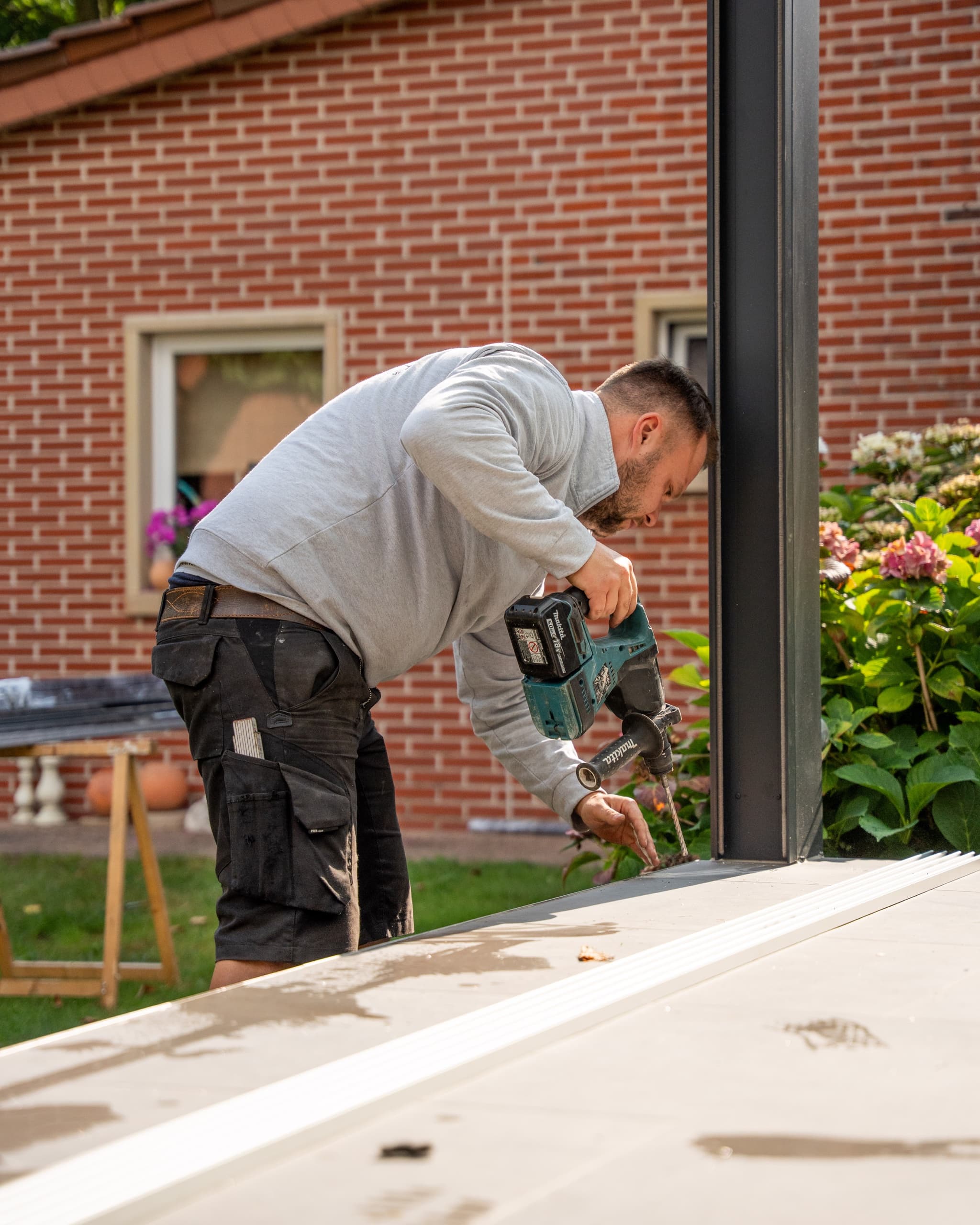 Terravista Meppen Monteur bohrt mit Makita-Bohrschrauber am Aluminium-Ständer der Terrassenüberdachung