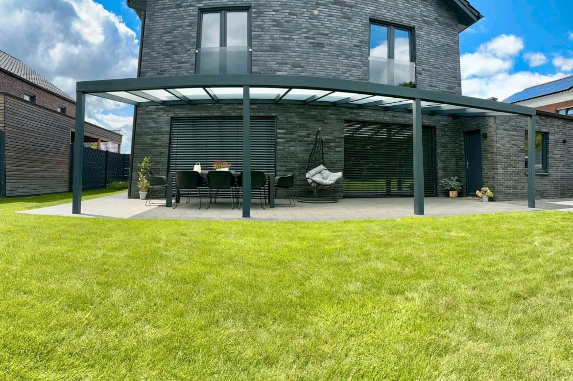 Anthrazitfarbene Terrassenüberdachung mit Glasdach über Sitzbereich und Hängestuhl an Backsteinhaus